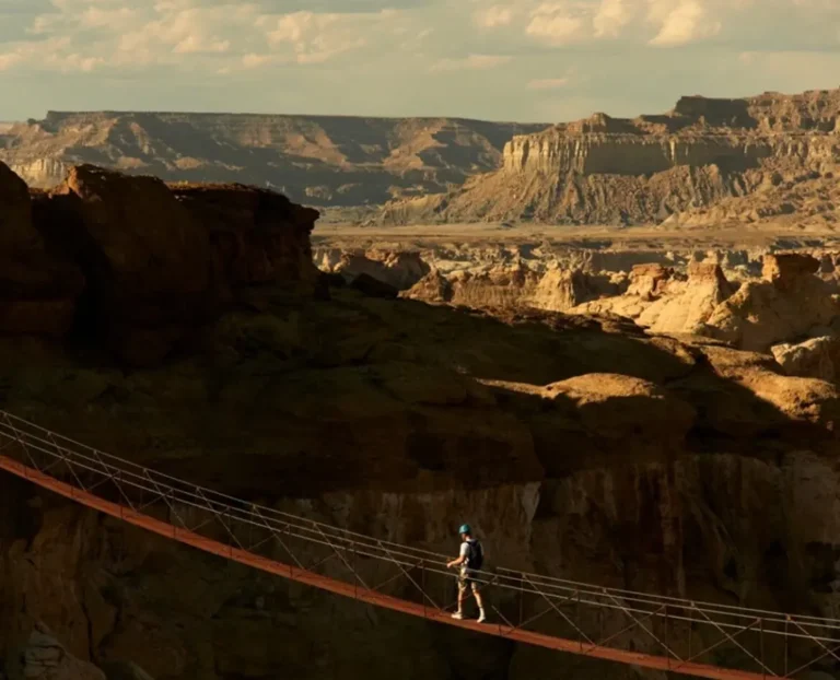 Traveler walking across suspension bridge over dramatic canyon landscape, adventure travel destination and scenic nature view.