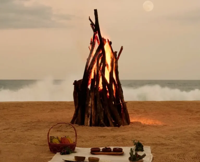 Romantic beach bonfire dinner setup by the ocean at sunset, luxury seaside dining experience and slow travel atmosphere.