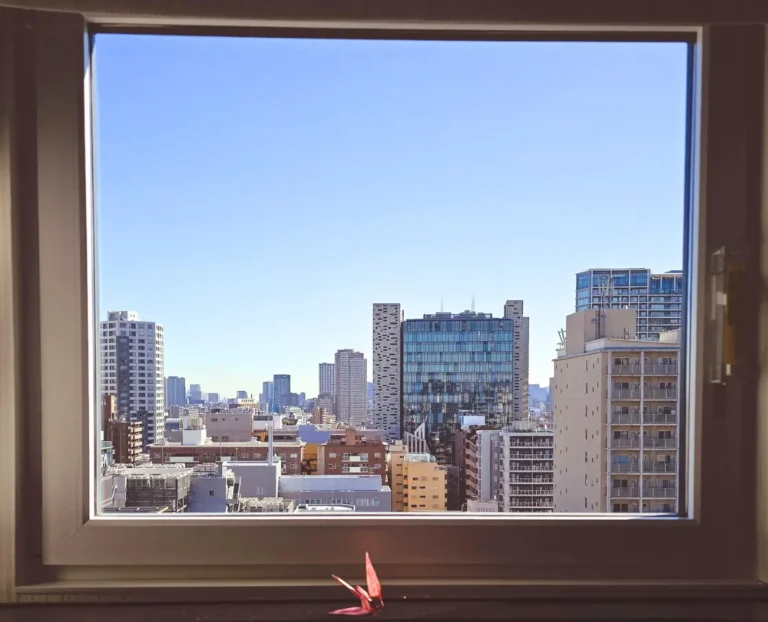 Modern city skyline view framed through hotel window, urban travel perspective from boutique hotel room.